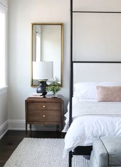 a bedroom with a bed, mirror and nightstand