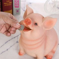 a small pig figurine is being given a coin by someone's hand