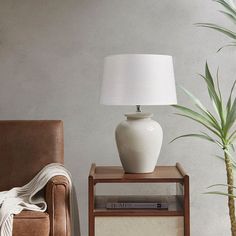 a white lamp sitting on top of a table next to a brown chair and potted plant