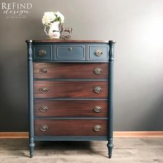 a dresser with flowers on top of it in front of a gray wall and wooden floor