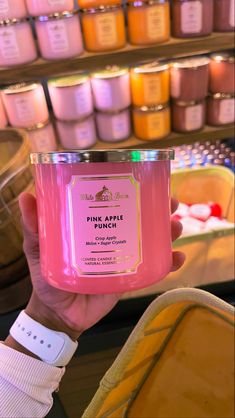 a person holding up a pink apple punch candle in front of some shelves filled with candles