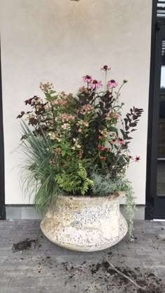 a planter filled with lots of flowers sitting on top of a cement floor next to a door