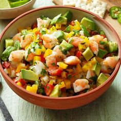 a bowl filled with shrimp, avocado and tomato salad on top of a table