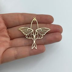 a person is holding a small gold bird brooch in their left hand, with the wings spread out