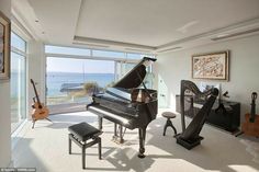 a living room filled with furniture and a piano in front of a large window overlooking the ocean