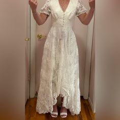 a woman is standing in front of a door wearing a white dress and holding her hands up