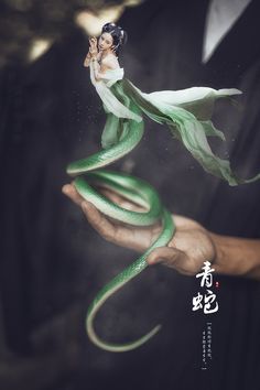 a person holding a green snake in their hand with chinese writing on the back ground