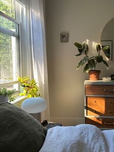 a bedroom with a bed, dresser and potted plant in the window sill