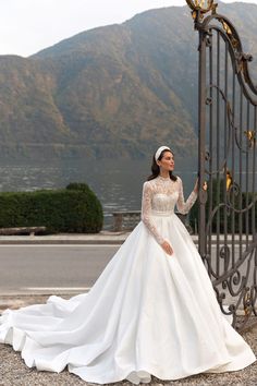 a woman in a wedding dress standing next to an iron gate with mountains in the background