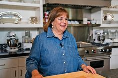 a woman standing in a kitchen next to a counter with a wooden board on it