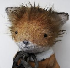 a stuffed animal with hair on it's head and clothes around its neck, sitting in front of a white wall