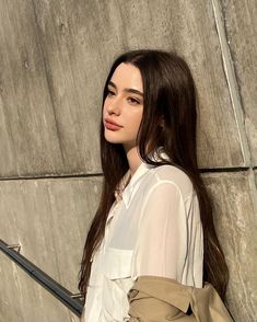 a woman standing next to a wall with a handbag on her shoulder and looking at the camera