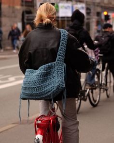 a woman riding a bike down the street with a crocheted bag on her back