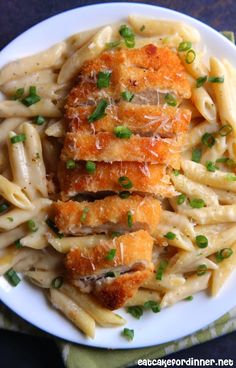 chicken parmesan with pasta and green onions on a white plate