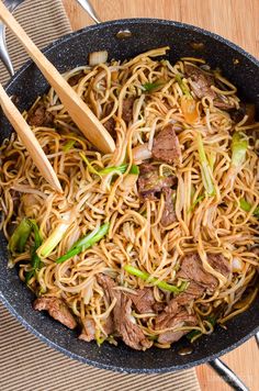 stir fried noodles with beef and vegetables in a skillet on a wooden table top