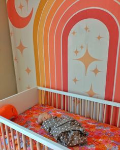 a baby in a crib next to a colorful wall