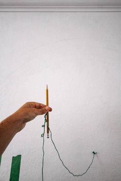 a person holding a pencil in their left hand and string attached to the wall behind them