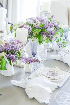 the table is set with purple flowers and white china plates, candles, and napkins