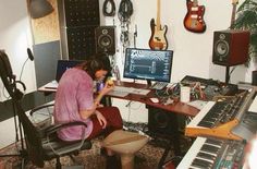 a woman sitting at a desk in front of a computer and musical equipment with guitars on the wall behind her