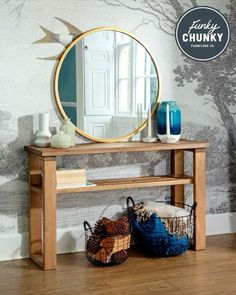 a wooden table with a mirror and baskets on it next to a wallpapered wall