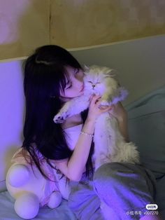 a woman holding a white cat on top of a bed next to a stuffed animal