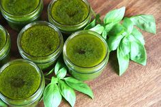 several jars filled with green liquid sitting on top of a wooden table next to leaves