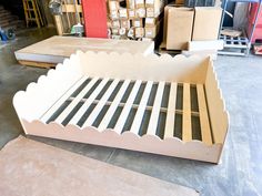 an unfinished bed frame with scalloped edges in a storage room filled with boxes