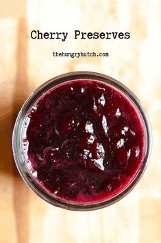 a glass filled with berry preserves on top of a wooden table