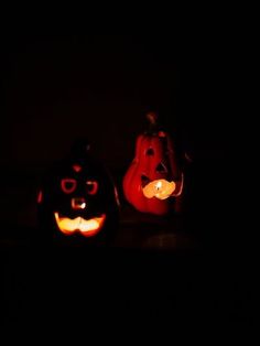 two pumpkins with faces carved into them in the dark, one is lit up