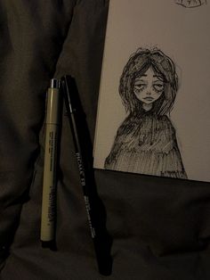 a drawing and pen on a bed next to a notepad with an image of a woman's face