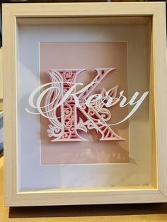 the letter k is made out of paper and framed in a white frame on a table