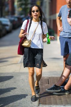 a woman walking down the street with a bottle in her hand and another man standing next to her