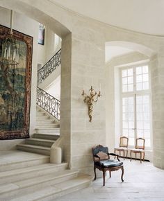 a chair sitting on top of a stone floor next to a stair case and chandelier