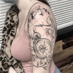 a woman with a tattoo on her arm has a compass and flowers in the background