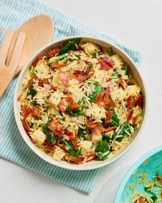 a bowl of pasta with bacon and spinach in it next to a wooden spoon