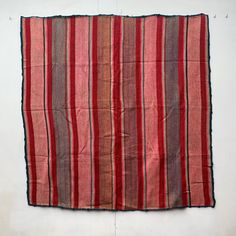 an old red and black striped cloth hanging on a white wall in the middle of a room