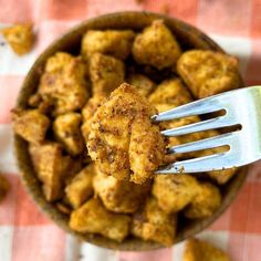 a fork in a bowl filled with tater tots on top of a checkered table cloth