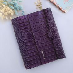 a purple crocd leather notebook sitting on top of a table next to flowers