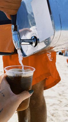 a person pouring something into a cup on the beach