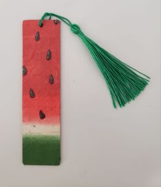 a watermelon bookmark with green tassels and black drops on it