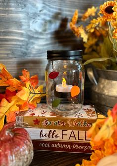 there is a candle in a glass jar on top of some books and fall leaves