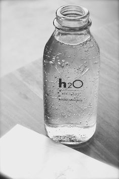 a bottle of water sitting on top of a wooden table next to a piece of paper