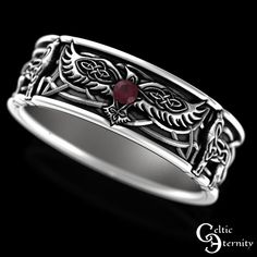 a silver ring with a red stone in the center and celtic designs on it's sides