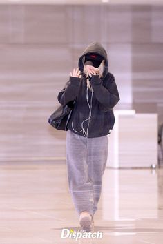 a woman walking through an airport while listening to headphones and wearing a hoodie