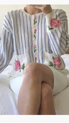 a woman sitting on top of a bed holding her hand to her face and looking at the camera