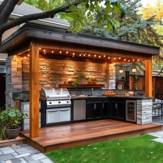 an outdoor kitchen and grill area with lights on the roof, surrounded by green grass