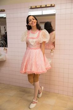 a woman standing in front of a bathroom mirror wearing a pink dress and white shoes