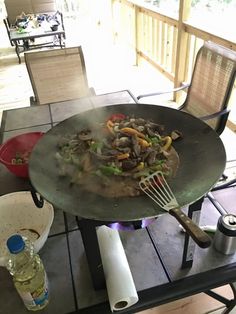 a wok filled with food sitting on top of a table next to two chairs