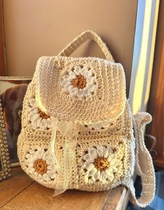 a crocheted bag with flowers on it sitting next to a mirror and framed photograph