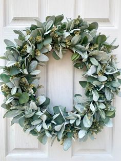 a wreath with green leaves hanging on a white front door, next to a wooden door